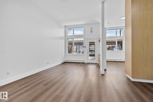 This expansive room features wide plank flooring and white walls, creating a bright and airy atmosphere - 116 11033 127 Street, Edmonton, AB - Indoor Photo Showing Other Room