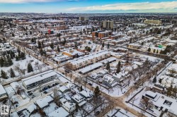 Aerial view of the surrounding neighbourhood featuring residential properties, trees, and roads, all covered in snow - 