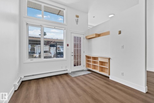 The entry area features modern wood-style flooring, a large window with additional transom windows, and a built-in storage unit with open shelving - 116 11033 127 Street, Edmonton, AB - Indoor Photo Showing Other Room