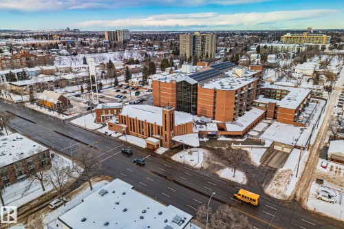 The property features a large multi-story building constructed with brick, situated in a developed area with numerous other buildings - 116 11033 127 Street, Edmonton, AB - Outdoor With View