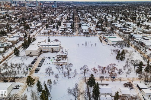 Aerial view of the surrounding neighborhood showcasing residential properties, tree-lined streets, and a large open field, all covered in snow - 116 11033 127 Street, Edmonton, AB - Outdoor With View
