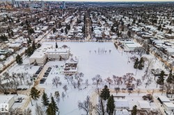 Aerial view of the surrounding neighborhood showcasing residential properties, tree-lined streets, and a large open field, all covered in snow - 
