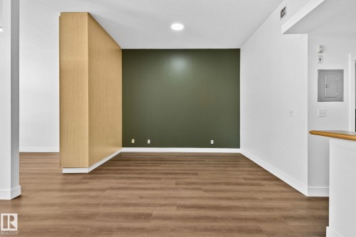 The property features wood-look flooring throughout, complemented by white walls and a distinctive dark green accent wall - 116 11033 127 Street, Edmonton, AB - Indoor Photo Showing Other Room