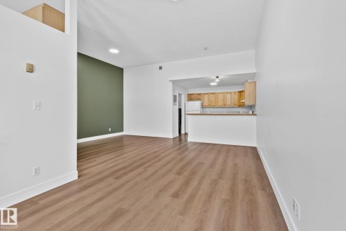 Spacious living area featuring light wood-style flooring and white walls, with a striking green accent wall - 116 11033 127 Street, Edmonton, AB - Indoor
