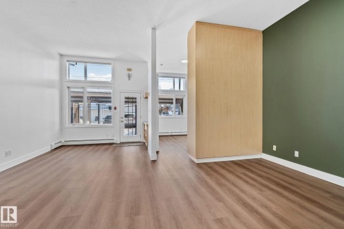 This spacious interior features rich wood-style flooring, white walls, and a contrasting accent wall in a deep green hue - 116 11033 127 Street, Edmonton, AB - Indoor Photo Showing Other Room