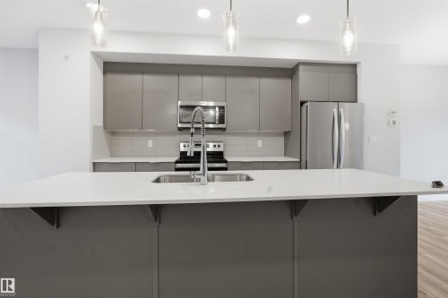 The kitchen features a large island with a double basin sink, stainless steel appliances, and sleek grey cabinetry - 40 1729 Keene Crescent, Edmonton, AB - Indoor Photo Showing Kitchen With Double Sink With Upgraded Kitchen