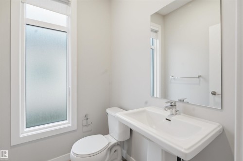 The bathroom features a pedestal sink with a modern faucet, a toilet, and a rectangular mirror - 40 1729 Keene Crescent, Edmonton, AB - Indoor Photo Showing Bathroom