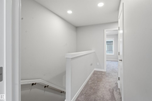 The property features a staircase with a white handrail and a carpeted hallway with a window providing natural light - 40 1729 Keene Crescent, Edmonton, AB - Indoor Photo Showing Other Room