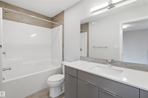 Bathroom featuring a bathtub and shower combination with tiled surround, a toilet, and a vanity with a white countertop and rectangular undermount sink - 40 1729 Keene Crescent, Edmonton, AB - Indoor Photo Showing Bathroom