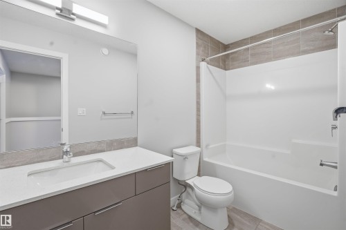 Bathroom featuring a single vanity with a white countertop, a mirror, and a shower-tub combination with tiled surround - 40 1729 Keene Crescent, Edmonton, AB - Indoor Photo Showing Bathroom