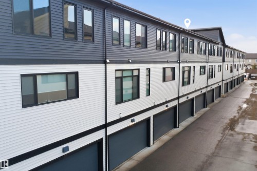 The property features a modern exterior with contrasting white and dark siding, numerous windows, and individual garage doors - 40 1729 Keene Crescent, Edmonton, AB - Outdoor With Exterior