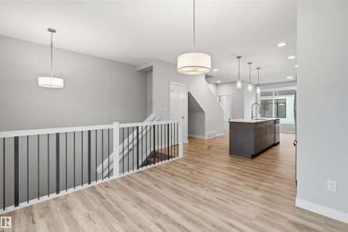 The property features light wood flooring, a staircase with white railings and black balusters, and a kitchen island with a light-colored countertop and dark cabinetry - 40 1729 Keene Crescent, Edmonton, AB - Indoor