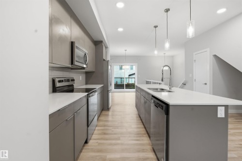 The kitchen features an island with a sink and pendant lighting, stainless steel appliances, modern cabinetry, and light-colored flooring - 40 1729 Keene Crescent, Edmonton, AB - Indoor Photo Showing Kitchen With Double Sink With Upgraded Kitchen