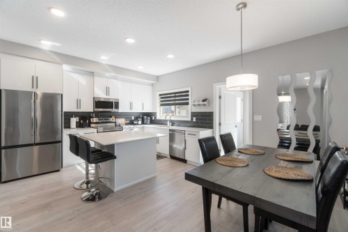 The kitchen features white cabinetry, stainless steel appliances, and a central island with a light-colored countertop - 29 Gambel Loop, Spruce Grove, AB - Indoor
