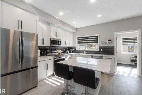 The kitchen features stainless steel appliances, white cabinetry with dark hardware, and a center island with a light-colored countertop - 29 Gambel Loop, Spruce Grove, AB - Indoor Photo Showing Kitchen With Double Sink With Upgraded Kitchen