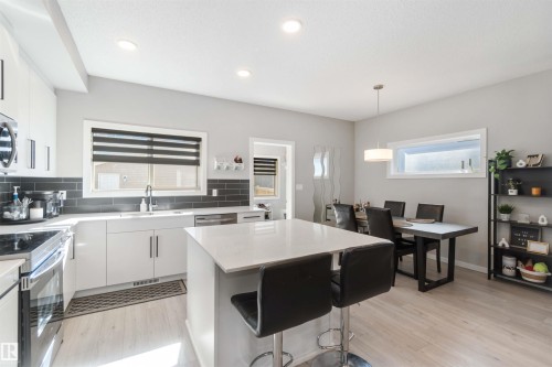 The kitchen features a center island with a light-colored countertop, white cabinetry with silver hardware, and stainless steel appliances - 29 Gambel Loop, Spruce Grove, AB - Indoor Photo Showing Kitchen With Double Sink