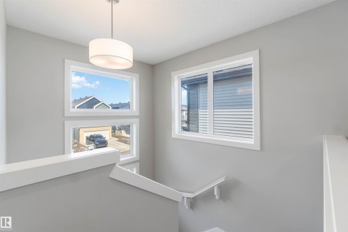 The property features windows providing natural light, a ceiling-mounted light fixture, and a staircase with a white handrail - 29 Gambel Loop, Spruce Grove, AB - Indoor Photo Showing Other Room