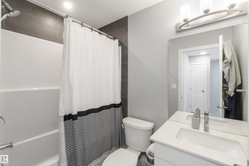 Bathroom featuring a shower and tub combination with dark tile surround, a white vanity with a rectangular sink, and a large wall mirror - 29 Gambel Loop, Spruce Grove, AB - Indoor Photo Showing Bathroom