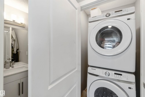 Convenient laundry area featuring a stacked washer and dryer, located near a bathroom with a vanity, sink, and mirror - 29 Gambel Loop, Spruce Grove, AB - Indoor Photo Showing Laundry Room