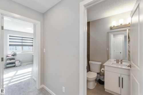 Hallway view of a bathroom featuring a vanity with a rectangular sink, a toilet, and a window in the adjacent room - 29 Gambel Loop, Spruce Grove, AB - Indoor Photo Showing Bathroom