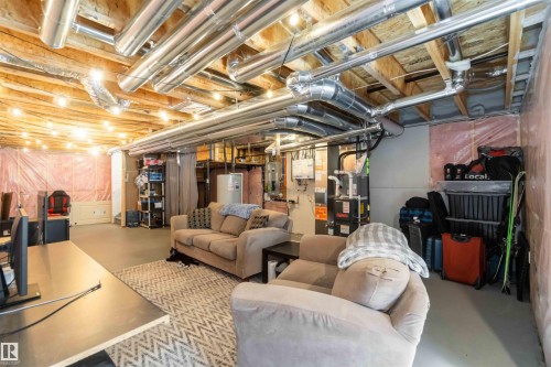 The basement features exposed ceiling joists and ductwork, with string lights providing illumination - 29 Gambel Loop, Spruce Grove, AB - Indoor Photo Showing Basement