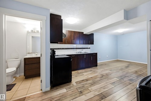 The property offers a kitchen area with dark wood cabinetry, a sink, and a tiled backsplash, and features light wood-style flooring throughout the main living space - 2812 16 Avenue, Edmonton, AB - Indoor