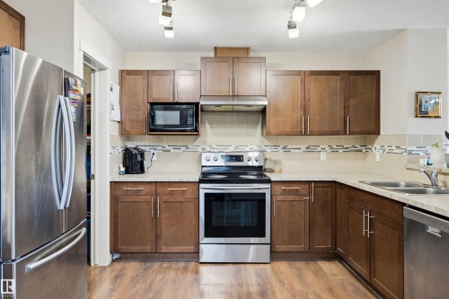 The kitchen features wooden cabinetry, stainless steel appliances, a tile backsplash, and light-colored countertops - 2812 16 Avenue, Edmonton, AB - Indoor Photo Showing Kitchen With Double Sink