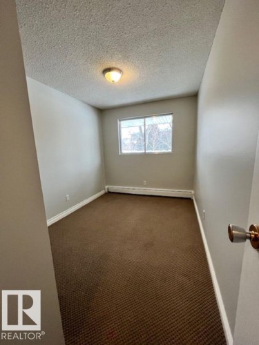 This room features neutral-toned walls, brown carpeting, and a window providing natural light - 4 10836 116 Street, Edmonton, AB - Indoor Photo Showing Other Room