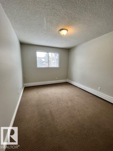 The room features neutral-toned carpet flooring, light-colored walls, and a window providing natural light - 4 10836 116 Street, Edmonton, AB - Indoor Photo Showing Other Room