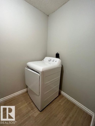 Laundry area featuring a top-load washing machine and a front-load dryer, with light-colored walls, a textured ceiling, and wood-look flooring - 4 10836 116 Street, Edmonton, AB - Indoor Photo Showing Laundry Room