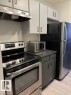 The kitchen features stainless steel appliances, including a range with an oven and an overhead ventilation hood, and a refrigerator - 4 10836 116 Street, Edmonton, AB  - Indoor Photo Showing Kitchen 