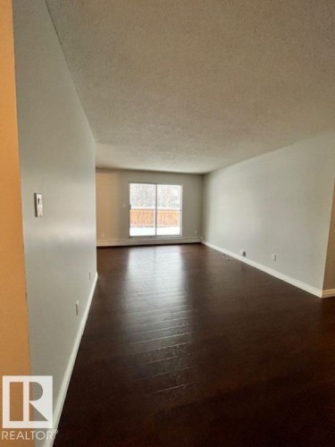 The property features dark wood flooring and light-colored walls, complemented by a large sliding glass door - 4 10836 116 Street, Edmonton, AB - Indoor
