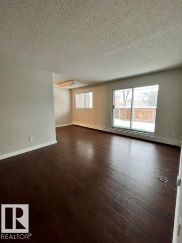 Living area featuring hardwood flooring, a window, and a sliding glass door leading to an outdoor space - 4 10836 116 Street, Edmonton, AB - Indoor Photo Showing Other Room