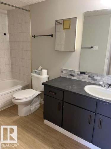 Bathroom featuring a bathtub with tiled walls, a dark vanity with a white sink and tiled backsplash, and light-toned flooring - 4 10836 116 Street, Edmonton, AB - Indoor Photo Showing Bathroom