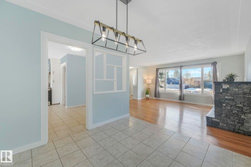 The property features an open living space with hardwood flooring, large windows, and a fireplace with a stone facade - 15704 91 Avenue, Edmonton, AB - Indoor Photo Showing Other Room