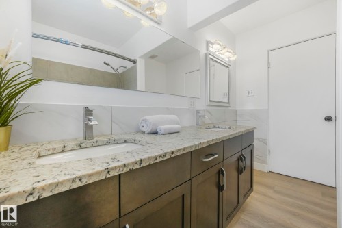 This bathroom features a double vanity with granite countertops and dark cabinetry, complemented by a large mirror and modern light fixtures - 15704 91 Avenue, Edmonton, AB - Indoor Photo Showing Bathroom