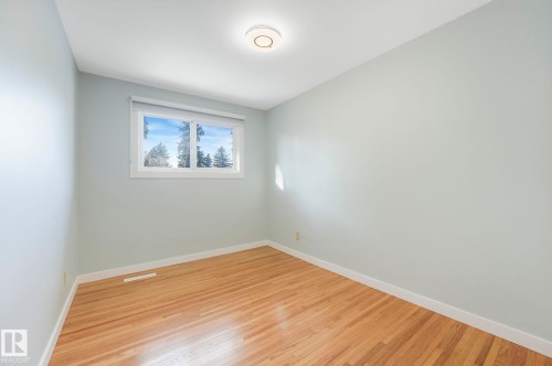 This room features light hardwood floors, light-colored walls, and a window providing natural light and views of trees and sky - 15704 91 Avenue, Edmonton, AB - Indoor Photo Showing Other Room