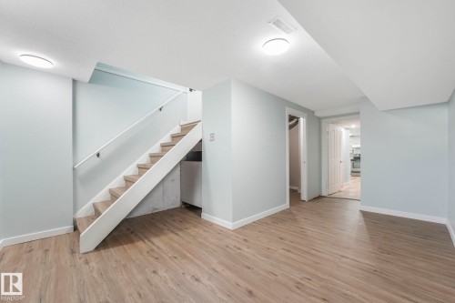 Spacious room featuring light wood-look flooring, light-colored walls, and a staircase with a white railing - 15704 91 Avenue, Edmonton, AB - Indoor Photo Showing Other Room