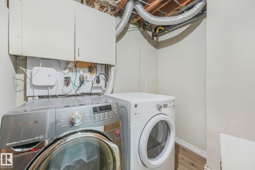 Dedicated laundry area featuring a front-loading washing machine and dryer, overhead cabinetry, and exposed ceiling ductwork - 15704 91 Avenue, Edmonton, AB - Indoor Photo Showing Laundry Room