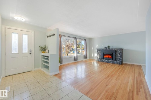 Entryway and living area featuring ceramic tile flooring, hardwood flooring, a stone fireplace, and large windows - 15704 91 Avenue, Edmonton, AB - Indoor With Fireplace