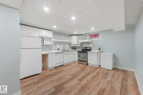 This kitchen features wood-look flooring, white cabinetry, and a stainless steel oven with a matching range hood - 15704 91 Avenue, Edmonton, AB - Indoor Photo Showing Kitchen