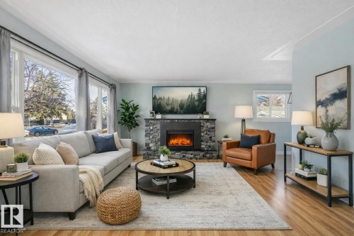 Living area featuring hardwood flooring, a stone fireplace, and large windows - 15704 91 Avenue, Edmonton, AB - Indoor Photo Showing Living Room With Fireplace
