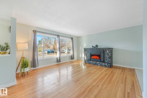 Living area featuring light-colored wood flooring, a stone-clad fireplace with an electric insert, and large windows providing natural light - 15704 91 Avenue, Edmonton, AB - Indoor Photo Showing Living Room With Fireplace