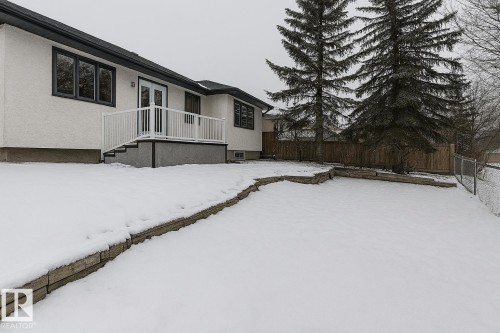 The property features a white exterior with dark trim windows, a white deck with railings and steps, and a spacious yard with mature evergreen trees - 9971 178 Avenue, Edmonton, AB - Outdoor