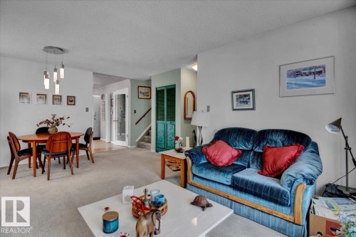 The living area features light-colored carpeting, white walls, and a modern chandelier illuminating the dining space - 3523 18A Avenue, Edmonton, AB - Indoor
