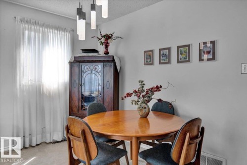 The dining area features a round wooden table, chairs with dark upholstery, and a statement chandelier with geometric lights - 3523 18A Avenue, Edmonton, AB - Indoor Photo Showing Dining Room