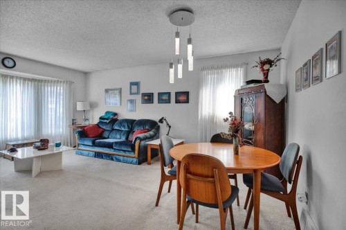 A bright living space featuring light-colored carpeting, a large bay window with white curtains, and a contemporary ceiling light fixture - 3523 18A Avenue, Edmonton, AB - Indoor
