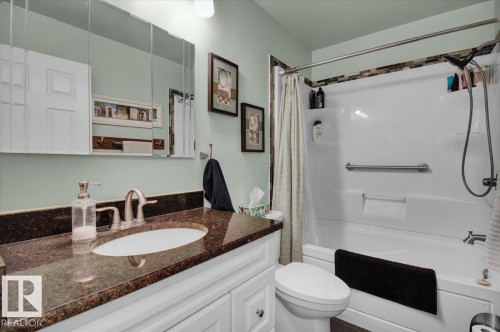 Bathroom featuring a vanity with a dark countertop and an undermount sink, a toilet, and a combination shower and tub with an accent tile border - 3523 18A Avenue, Edmonton, AB - Indoor Photo Showing Bathroom