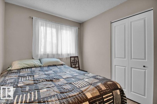 This room features neutral-toned walls, a window with sheer white curtains, and a bi-fold closet with white paneled doors and dark hardware - 3523 18A Avenue, Edmonton, AB - Indoor Photo Showing Bedroom