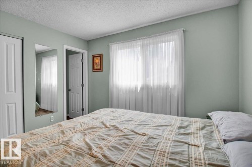 This room features light green walls, a window with sheer white curtains, and a white six-panel door - 3523 18A Avenue, Edmonton, AB - Indoor Photo Showing Bedroom